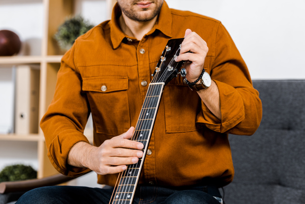 обрізаний вид людини, що налаштовує акустичну гітару вдома
 - Фото, зображення