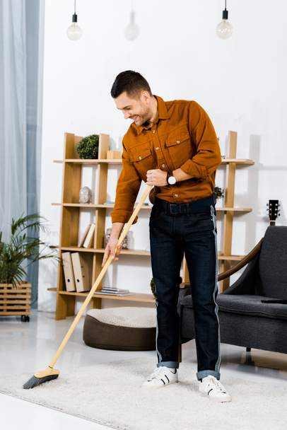 jóképű férfi, seprű-a modern nappali szőnyeg takarítás  - Fotó, kép