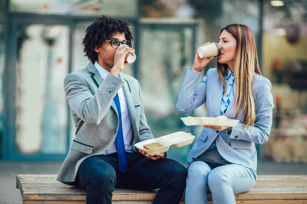 Empresários sorridentes com sanduíches sentados em frente ao prédio de escritórios - pausa para almoço, foco seletivo
. - Foto, Imagem