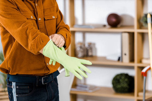 cropped view of man standing in modern living room putting up rubber gloves - Photo, Image