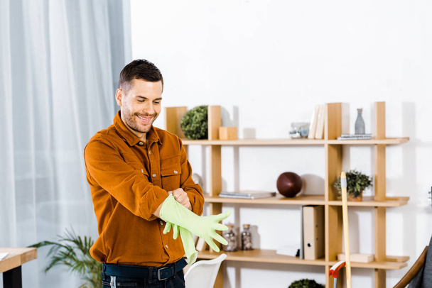 handsome man standing in modern living room and putting up rubber gloves - 写真・画像