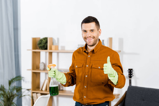 smiling man in modern living room doing thumb up gesture and holding bottle - Photo, image