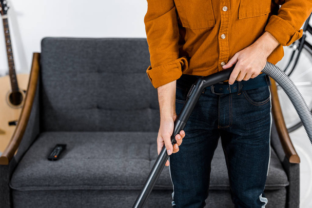 cropped view of man in modern living room cleaning floor with hoover  - Photo, Image