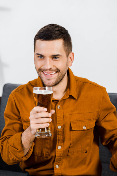 handsome man in modern living room sitting on sofa and holding glass of beer - Zdjęcie, obraz