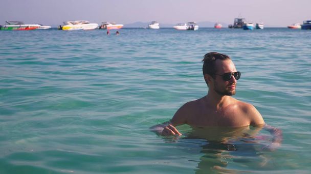 Portrait of a handsome young man with a beard in sunglasses relaxed in crystal clear sea water - Valokuva, kuva