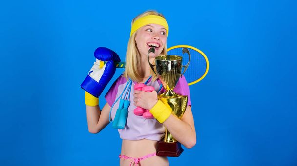 How to find time for everything. Sport equipment store. Sport for every day. Sport shop assortment. Girl successful modern woman hold golden goblet of sport champion and equipment blue background - Foto, Imagen