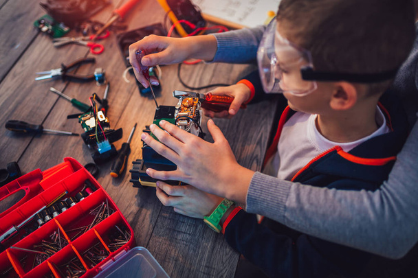 Onnellinen hymyilevä poika ja tyttö rakentaa teknisen lelun ja tehdä robotti. Tekninen lelu pöydällä täynnä yksityiskohtia
 - Valokuva, kuva