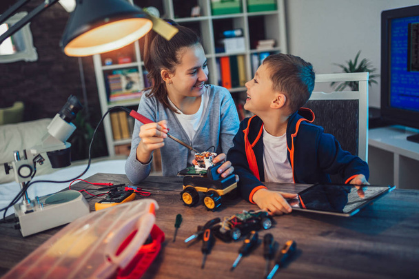 Счастливый улыбающийся мальчик и девочка конструируют техническую игрушку. Техническая игрушка на столе с деталями
 - Фото, изображение