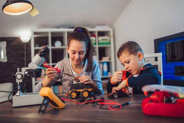 Счастливые улыбчивые мальчик и девочка, техническая игрушка и робот. Техническая игрушка на столе с деталями
 - Фото, изображение