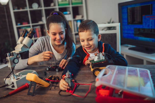 Ευτυχισμένος χαμογελαστό αγόρι και κορίτσι κατασκευάζει τεχνικά ρομπότ παιχνίδι και να κάνουν. Τεχνικών παιχνιδιών σε τραπέζι γεμάτο λεπτομέρειες - Φωτογραφία, εικόνα