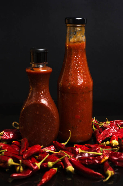Bund getrockneter Chilischoten und Flaschen roter würziger Sauce - Foto, Bild