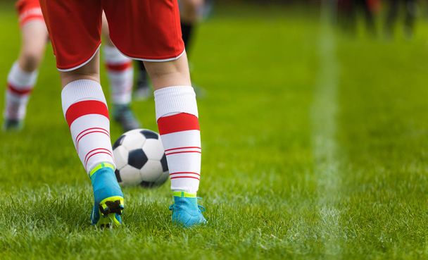 Detail Soccer Background. Close up legs and feet of football player in white socks and blue cleats playing game on green grass pitch. Footballers in red jersey uniforms kicking soccer training match - Fotografie, Obrázek