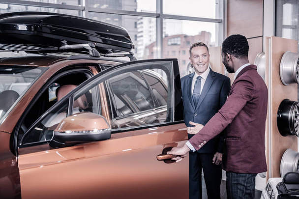 Sales manager wearing dark red jacket opening door of car for his client - Fotoğraf, Görsel