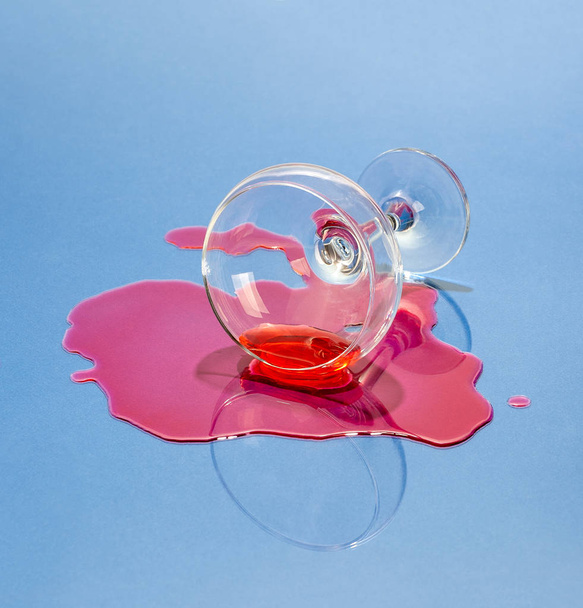 A glass and spilled liquor on a light blue background. Art photo - Foto, afbeelding