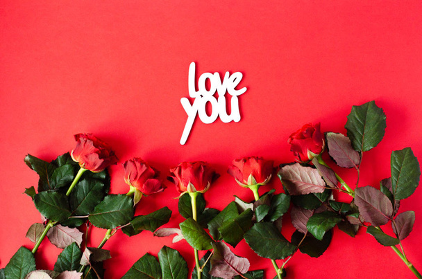Rosas com uma inscrição de madeira amam você em um fundo vermelho
. - Foto, Imagem
