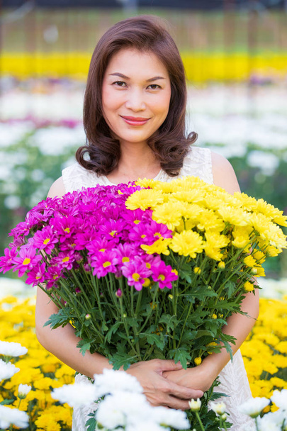 Beautiful Asian woman holding yellow flowers in hands with pride manner, flower garden owner satisfied with good quality flowers for sale. - Photo, Image