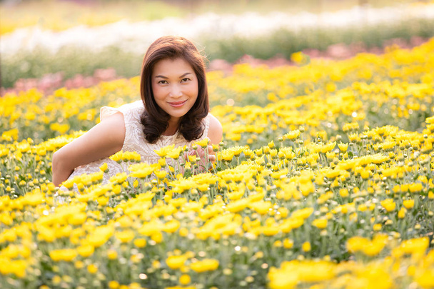 Schöne asiatische Frau steht und lächelt in tropischen Blumengarten mit glücklichen Weise mit warmem Sonnenlicht aus dem Hintergrund. - Foto, Bild