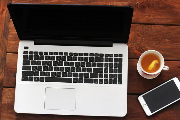 Laptop, phone and tea on wooden background - Fotó, kép
