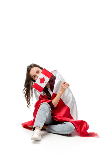 女性は、白で隔離の顔の前にカエデの葉の旗を保持しているカナダの国旗で覆われています。 - 写真・画像