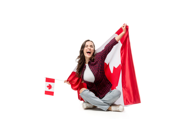 excited woman covered in canadian flag holding maple leaf flag isolated on white - 写真・画像
