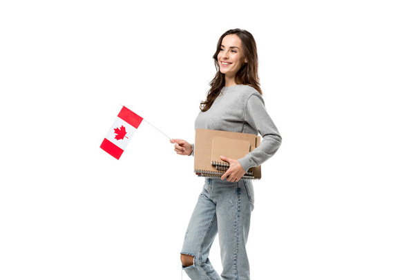 lachende vrouwelijke student houden van de Canadese vlag en notebooks geïsoleerd op wit - Foto, afbeelding