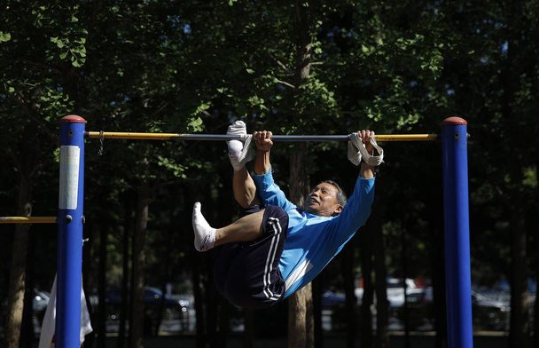 68-year-old Chinese man Nie Yinmin binds and fixes his feet on a horizontal bar to complete 360-degree rotations at a park in Shenyang city, northeast China's Liaoning province, 20 May 2018 - Photo, Image