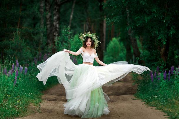 die Braut in einem schönen weißen Kleid und einem Kranz aus Waldblumen - Foto, Bild