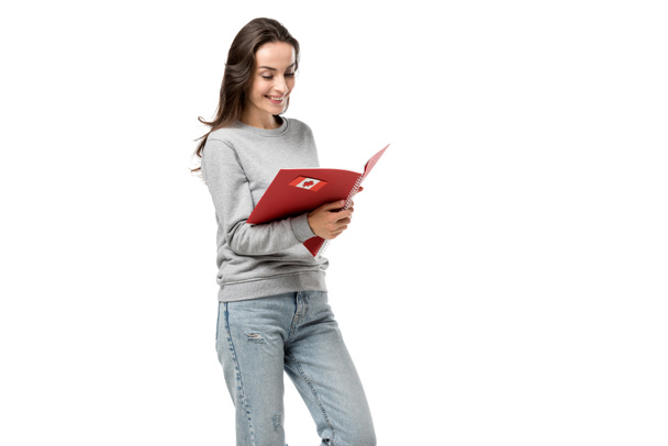 female student looking at red notebook with maple leaf sticker isolated on white - Photo, Image