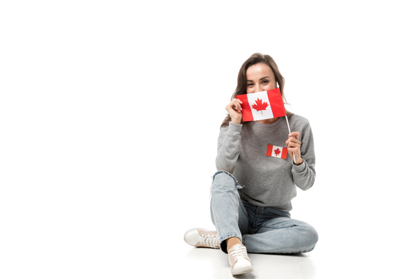 žena s maple leaf odznak sedí a drží kanadské vlajky izolované na bílém - Fotografie, Obrázek