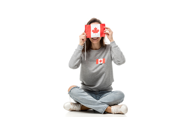woman with maple leaf badge sitting and holding canadian flag in front of face isolated on white - Photo, Image