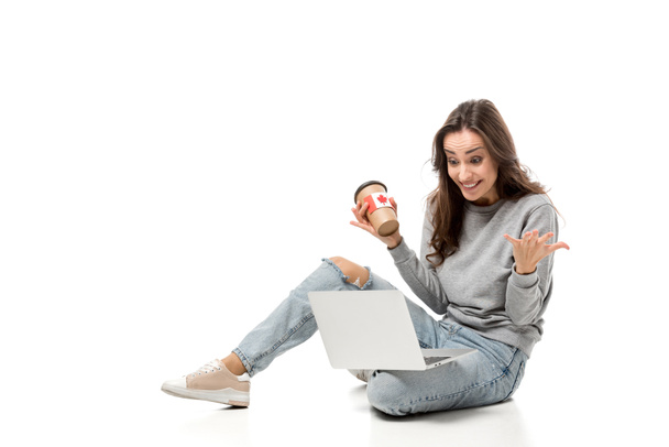 mujer sorprendida usando el ordenador portátil y sosteniendo la taza de café con etiqueta engomada bandera canadiense aislado en blanco
 - Foto, Imagen