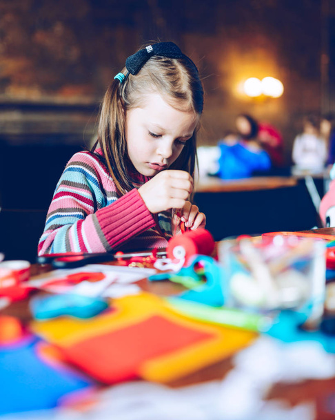 Krawiec warsztaty artystyczne dla dzieci - dziewczyna szycia dekoracje - kolorowe tkaniny leżące na stole - mała dziewczynka poślizgiem igły z filcu - Zdjęcie, obraz