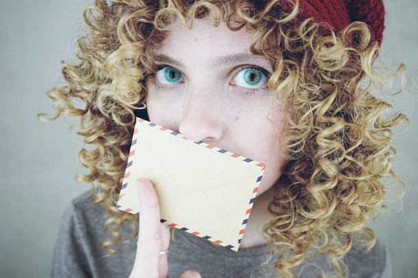 Portrait de gros plan d’une belle et jeune femme drôle aux yeux bleus et cheveux blonds bouclé avec une lettre, elle se méfie du message - Photo, image