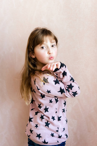 Meisje met lang donker blond haar en prachtige expressieve bruine ogen op roze achtergrond Toon lucht kus. Kleine dame schoolmeisje 8 jaar oud. - Foto, afbeelding