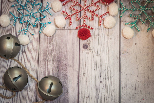 Pom pom νιφάδες χιονιού ύφασμα νήματος σε χρώματα λευκό, κόκκινο και κιρκιριών, με μεγάλη ασημένια κουδουνάκια. Ξύλινο υπόβαθρο, χρήσιμο για αγροτικά προγράμματα διακοπών Χριστουγέννων - Φωτογραφία, εικόνα