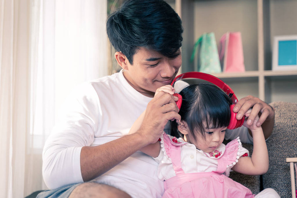 Parent giving headphones to little daughter listening the music . Happy family spending time together. - Photo, Image