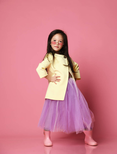 Μικρό ασιατικό κορίτσι σε κίτρινο μόδα ζακέτα μοβ φόρεμα και μοντέρνα κόκκινα γυαλιά ηλίου που παρουσιάζουν - Φωτογραφία, εικόνα