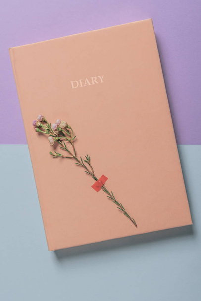 Diario e fiore bianco primaverile incollato sulla sua copertina. Immagine laica piatta con un diario su sfondo bicolore
 - Foto, immagini