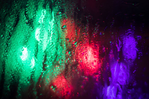 Pozadí, barevné světelné skvrny viditelné skrz mokré sklo ve tmě, když prší. Noční cesta v dešti - Fotografie, Obrázek