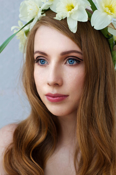 Portrait of a tender girl in a wreath of narcissus, spring freshness, light background - Fotó, kép