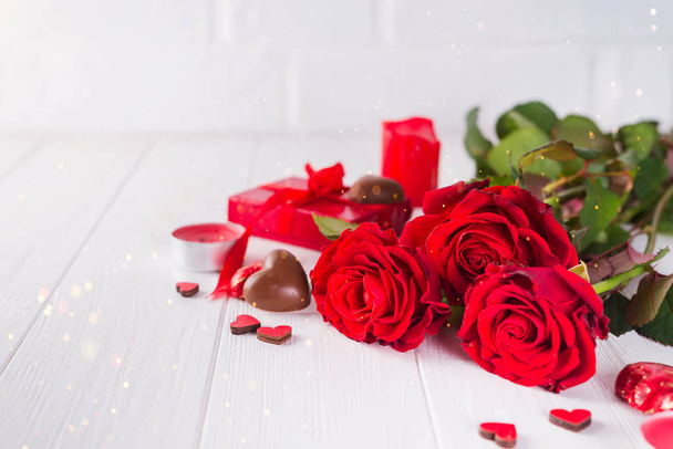 Цукерки у формі цукерок у формі серця з подарунковою коробкою на білому дерев'яному фоні з червоними трояндами
 - Фото, зображення