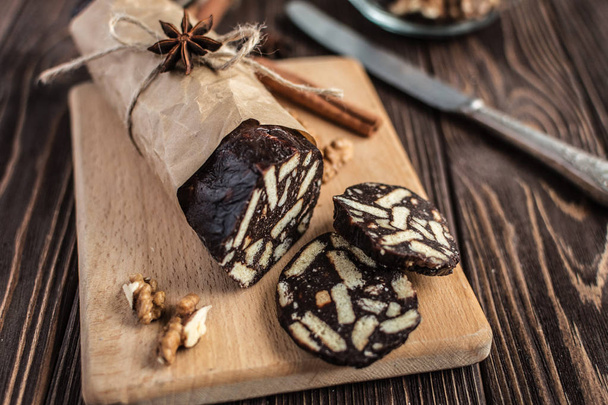 Chocolate sausage on a wooden background. Dessert made of biscuits, chocolate and nuts is sliced on a wooden board - Φωτογραφία, εικόνα