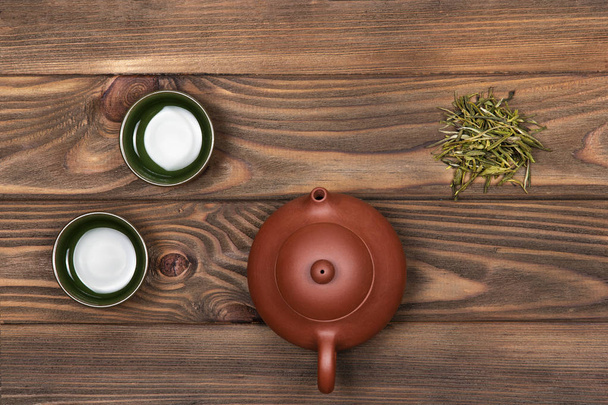 Tetera de cerámica marrón, dos tazas especiales de color verde oscuro y té verde sobre un fondo con tablones de madera oscura. Ceremonia del té
.  - Foto, imagen