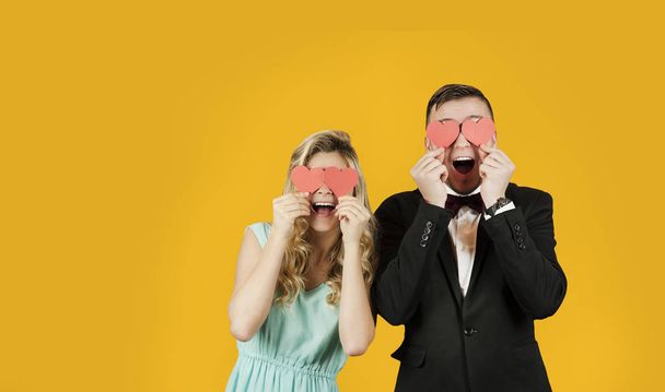 Young romantic beautiful couple in love with a girl with a girl with red hearts in their hands on a yellow isolated background. Valentine's Day concept. Valentine's Day - Foto, Imagen