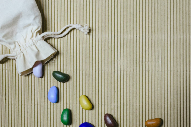 Background of colored fake stones scattered on a wavy paper with cloth sachet. - Photo, Image