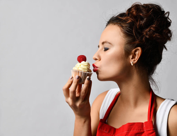 Young woman chef cook hold sweet cup cake with cream and strawberry happy looking at the corner  - Fotoğraf, Görsel