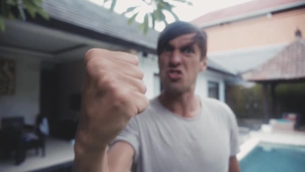Agresywny mężczyzna krzyczy i grozi pięścią na tle domu w jego stoczni. Groźby przemocy - Materiał filmowy, wideo