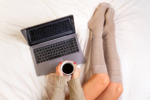 Pehmeä kuva naisesta sängyllä kannettava tietokone ja kuppi kahvia käsissä, ylhäältä katsottuna
 - Valokuva, kuva