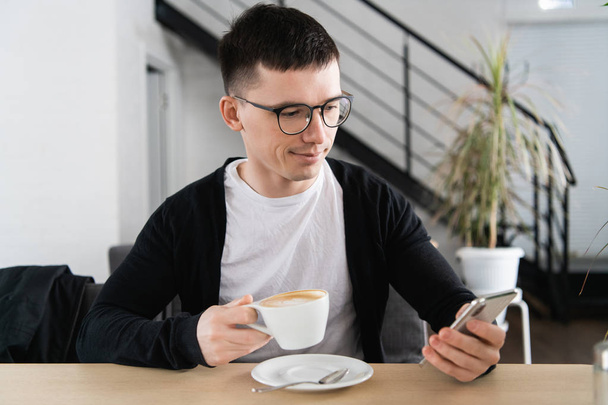 Handsome man having coffee and using smartphone at coffee shop - Fotó, kép