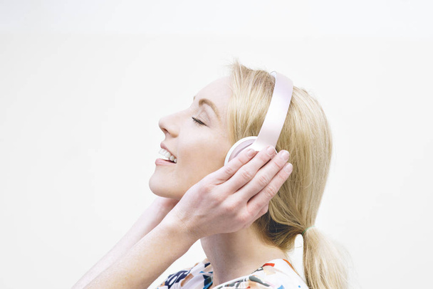 Blond female millennial listens to music on headphones and is inspired against a plain background - Foto, Imagen